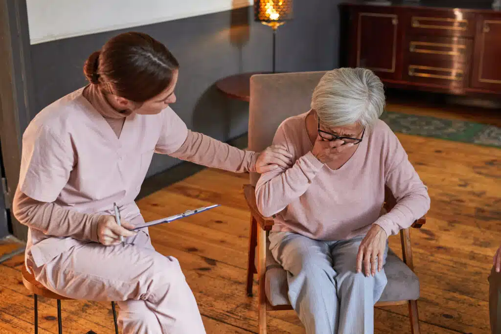 Portrait of young woman comforting crying senior lady during therapy session at retirement home, copy space